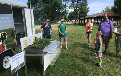 Two staff standing nest to soil samples with different land management types. Crowd looking at samples.