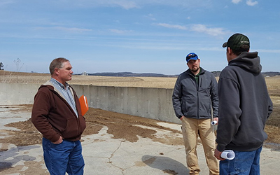 Three people stand in front of a large concrete basin.