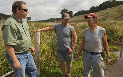 Three people next to a farm stream talking.