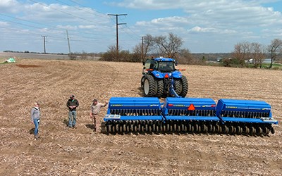 Aerial image of three people talking in a field with a large blue farm tractor next to them.