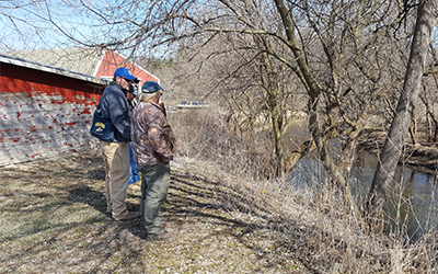 Staff member with two landowners standing at the top of a streambank looking toward the water.