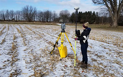 Staff member with bright yellow survey equipment standing in a snowy field.
