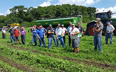 A large group of people standing in a farm field looking at a crop