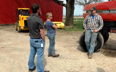 Three people talking in a farm yard next to tractor.