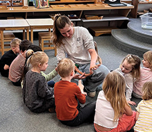 Staff member holding a corn snake with little kids sitting on the floor in front