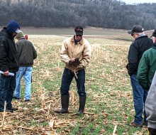 A man holding soil talking with other people in a farm field.